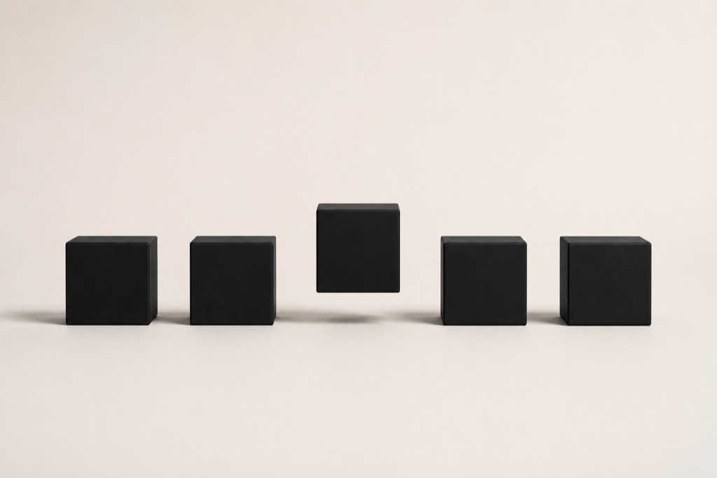 Cinco cubos idênticos de preto fosco numa fila precisa sobre fundo branco-osso; um elevado acima da linha