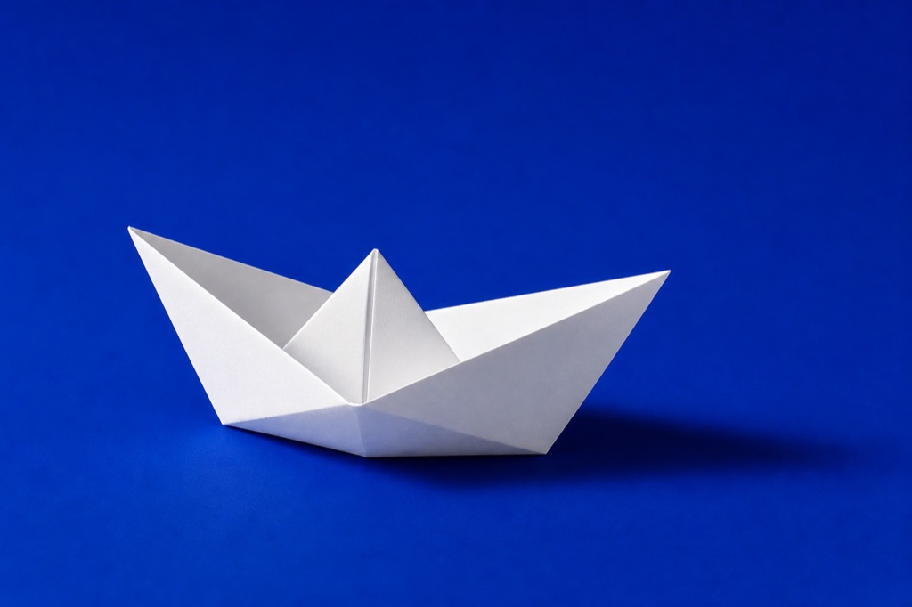 Barco de papel branco dobrado sobre fundo azul Klein vibrante